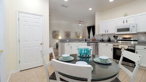 A modern kitchen with white cabinets, a microwave, an oven, and a dining area with a glass table and chairs. - Stunning 4BR Disney Villa w/ Pool & Arcade (Clermont)