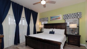 A bedroom with a large bed, a ceiling fan, a nightstand with a lamp, and a window with blinds. - Stunning 4BR Disney Villa w/ Pool & Arcade (Clermont)