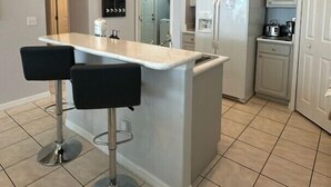 Una cocina moderna con una isla central, dos taburetes de bar, un refrigerador y un lavabo.