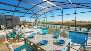An outdoor pool area with tables and chairs, a covered seating area, and a view of a body of water and landscape. - 6-Bedroom Home with Private Pool, Spa & Game Room (Davenport)