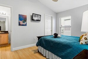 Quarto com cama, televisão, porta e janela com persianas.