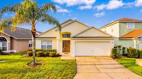 A residential house with a garage, a front yard with a palm tree, and a clear blue sky.