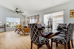 A modern dining area with a glass table, patterned chairs, and a ceiling fan.