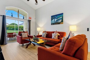 A modern living room with a glass coffee table, orange sofas, and a painting of boats on the wall.