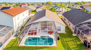 A residential property with a swimming pool, covered outdoor seating area, and a view of neighboring houses.