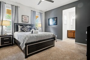 Une chambre à coucher comprenant un lit, des tables de chevet, un ventilateur de plafond et donnant sur la salle de bain.
