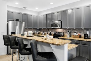 Una cocina moderna con electrodomésticos de acero inoxidable, encimeras de granito y taburetes de bar.