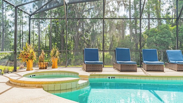 Un espace piscine doté d'une structure en verre, de fauteuils de relaxation en osier et de plantes en pot.