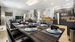 Une cuisine moderne équipée d’appareils électroménagers en acier inoxydable, un coin repas avec une longue table pouvant accueillir six personnes, et un escalier menant à l’étage supérieur.