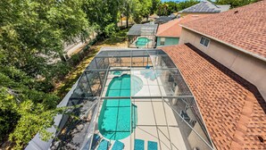 Une piscine sur le toit, protégée par une structure en verre, entourée d’arbres et bordée d’immeubles.