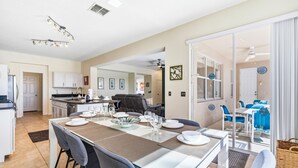 Une cuisine moderne avec des meubles blancs, un coin repas doté d’une table en verre, et une vue sur un salon avec un canapé bleu.