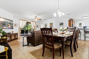 A dining area with a table set for four, surrounded by wooden chairs, a ceiling fan, and a chandelier.