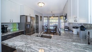 A kitchen with white cabinets, a granite countertop, stainless steel appliances, and a dining area with a table and chairs.