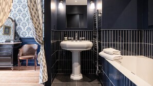 A bathroom with a pedestal sink, a mirror above it, and a bathtub with towels. - Deluxe double room (Le Pian-Médoc)