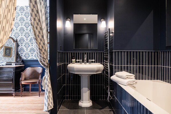 A bathroom with a pedestal sink, a mirror above it, and a bathtub with towels.