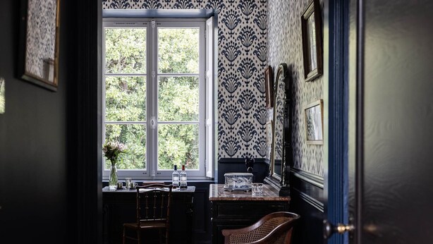 A room with a large window, a desk with a vase of flowers, and a chair. - Deluxe double room (Le Pian-Médoc)