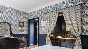 A bedroom with patterned wallpaper, a bed, a chair, a desk, and a wardrobe. - Deluxe double room (Le Pian-Médoc)