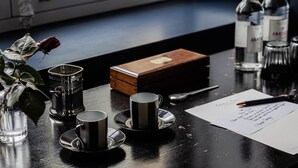 A table with three cups and saucers, a rose in a glass, a box, and a pen on a black table. - Deluxe double room (Le Pian-Médoc)
