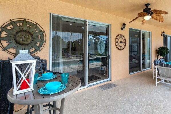 A patio area with a table set for dining, a decorative sun sculpture, a wall clock, and a ceiling fan.