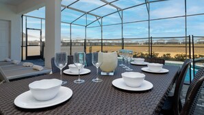 Una mesa de comedor dispuesta con cuencos blancos y copas de vino, con vistas a una piscina y un campo.