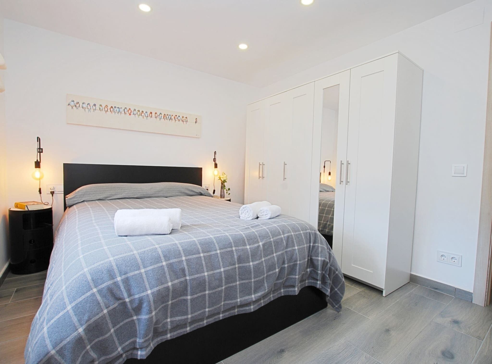 Un dormitorio con cama, mesitas de noche, armario y una obra de arte en la pared.