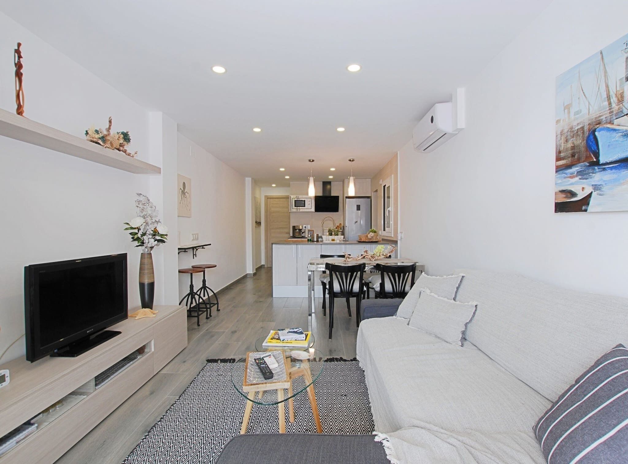 A modern living room with a flat-screen TV, a sofa, and a dining area with chairs and a table.