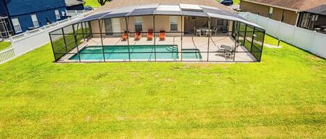 A backyard with a swimming pool, covered patio, and lawn chairs.