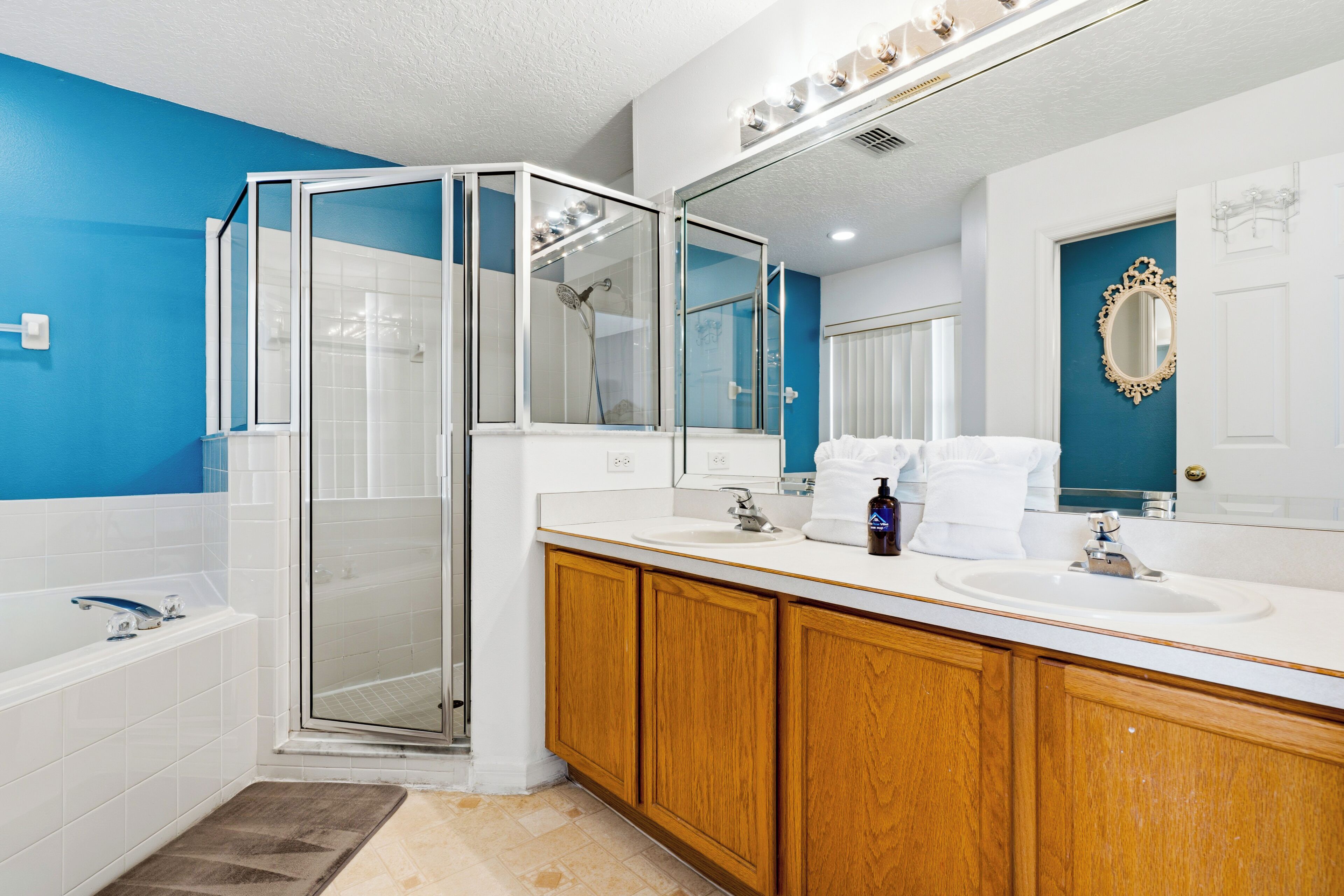 A modern bathroom with a glass-enclosed shower, wooden cabinets, a large mirror, and a blue accent wall.