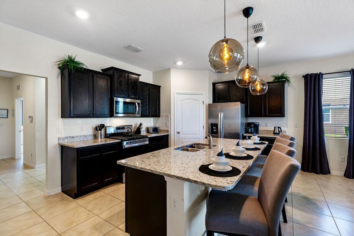A modern kitchen with dark cabinetry, granite countertops, a central island, and pendant lighting.