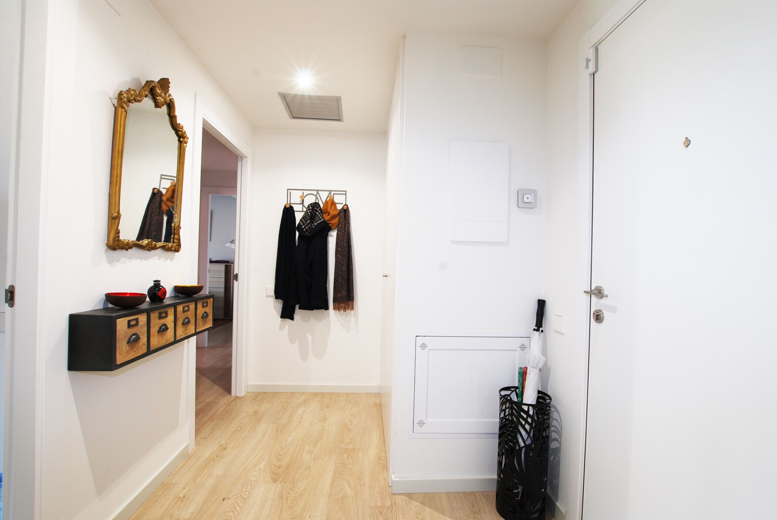 Un couloir avec un miroir, un porte-manteau et un radiateur.