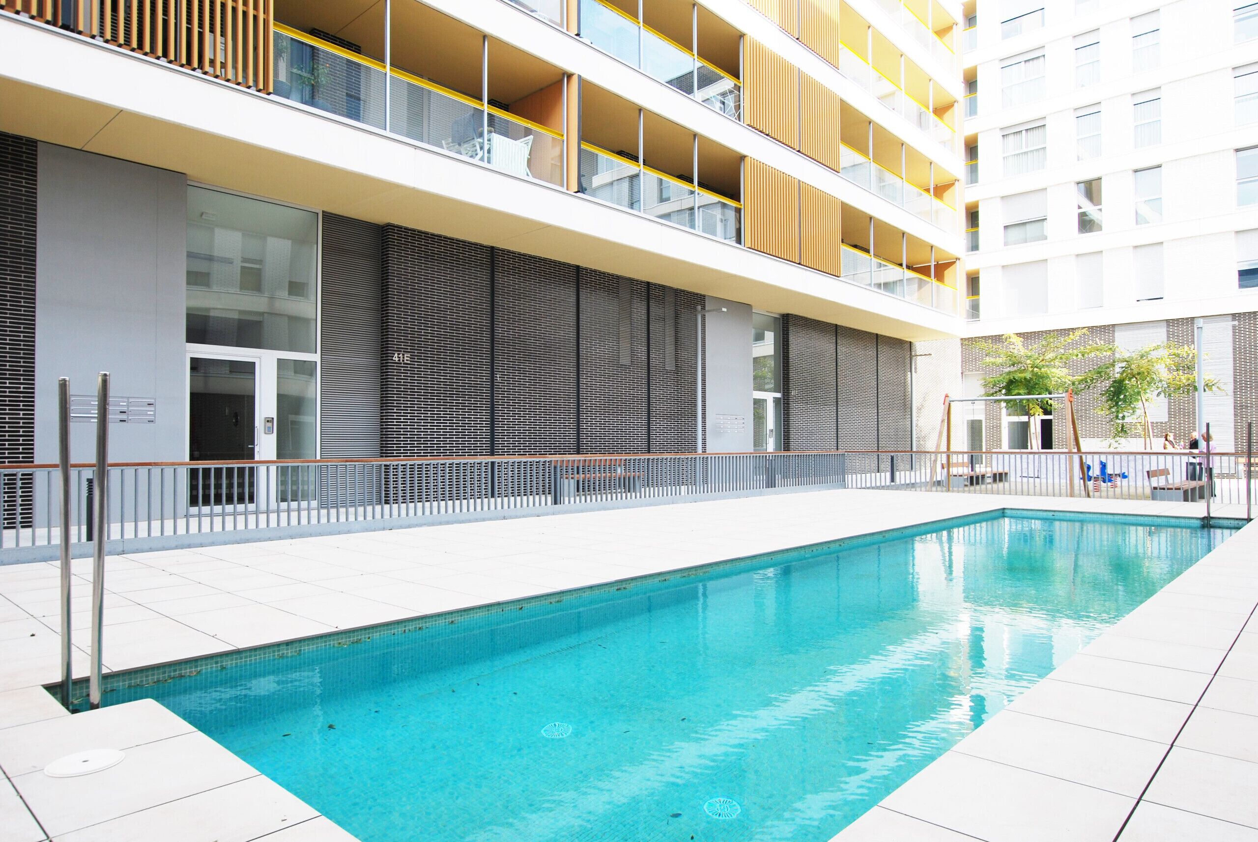 A modern building with a swimming pool, balconies, and a gated entrance.