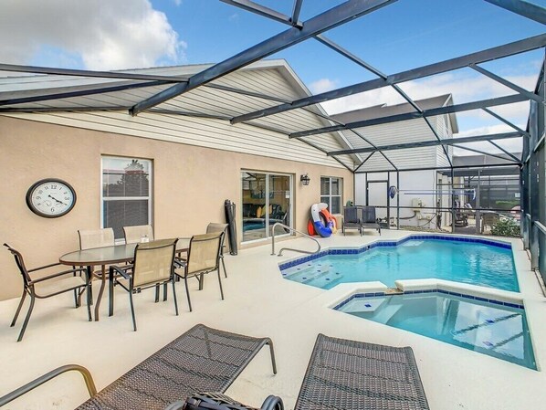 An outdoor pool area with a covered patio, lounge chairs, and a dining table.