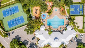 An aerial view of a sports complex with multiple tennis courts, a swimming pool, and a covered seating area.