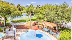A playground with a blue rubberized surface, surrounded by trees and a fenced area.