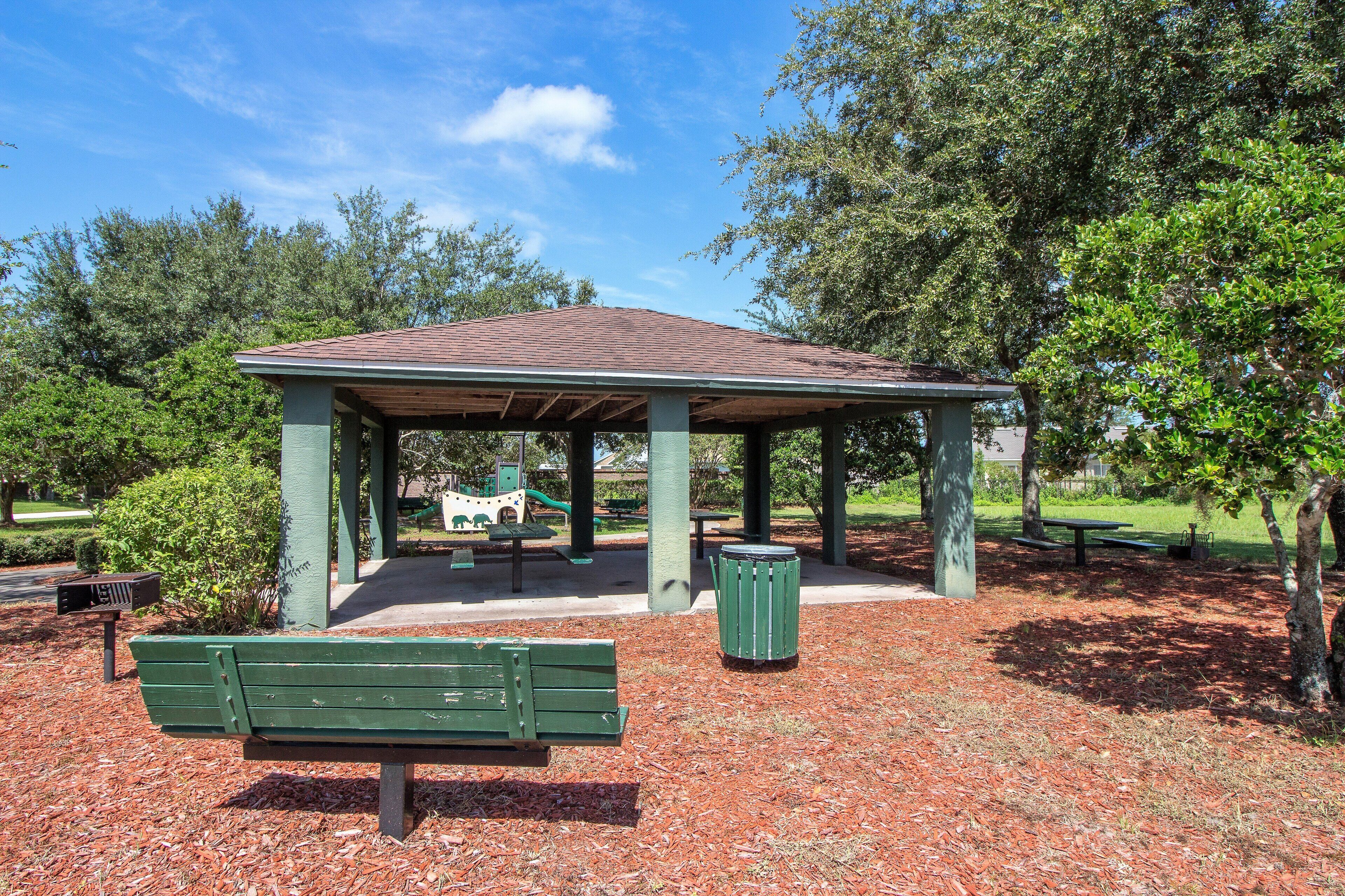 Un pavillon abrité avec un banc et une poubelle dans un parc.