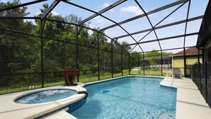A swimming pool with a hot tub, surrounded by a covered area with a view of trees.