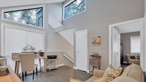 A spacious living area with a high ceiling, a staircase, and a view of trees through large windows. - 265 Turnberry @ Palmetto Dunes | Golf View Escape | Walk to Beach | Pool, Golf & Tennis (Hilton Head Island)