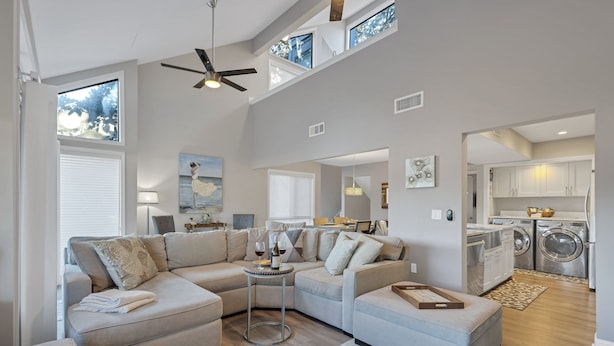 A modern living room with a sectional sofa, a small round table, and a kitchen area with a washing machine. - 265 Turnberry @ Palmetto Dunes | Golf View Escape | Walk to Beach | Pool, Golf & Tennis (Hilton Head Island)