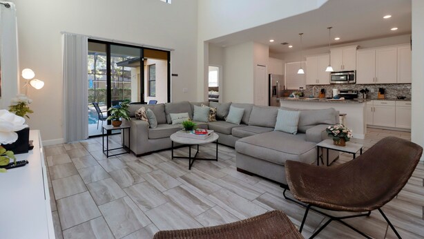 A spacious living area with a grey sofa, a round coffee table, and a brown chair. A kitchen with white cabinets and a microwave is visible in the background. - Modern 5BR Oasis w/ Pool, Spa & Resort Perks (Davenport)