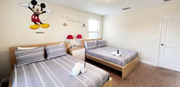 Habitación de hotel con dos camas individuales, un adhesivo de pared de Mickey Mouse, una ventana con persianas y una puerta blanca.