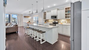 Una cocina moderna con armarios blancos, una isla central con taburetes altos, iluminación colgante y un microondas integrado.
