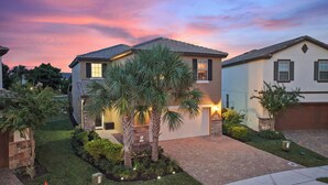 A residential house with a two-story design, a brick driveway, and a well-maintained garden with palm trees. - Ultimate Pool Villa | Theater, Arcade & Fun (Davenport)