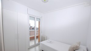 A white room with a bed, a wardrobe, and a sliding door to a balcony.