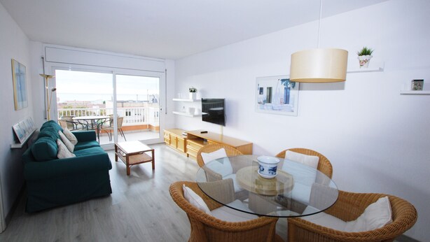 A modern living room with a glass dining table, wicker chairs, a green sofa, and a TV on a wooden cabinet.