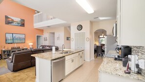 A modern kitchen with a central island, white cabinetry, and a dining area with a brown leather couch. - Disney Villa Free BBQ, Pool & Game Room (Davenport)