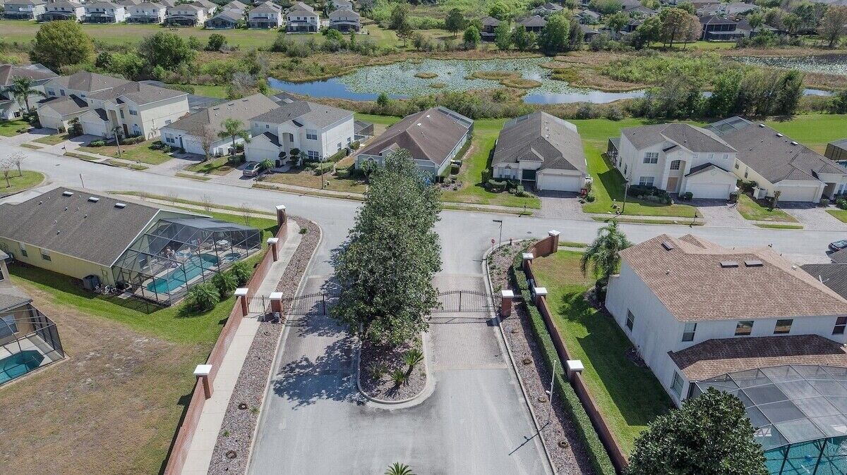 Vista aérea de un barrio residencial con casas, una calle central y un pequeño estanque.