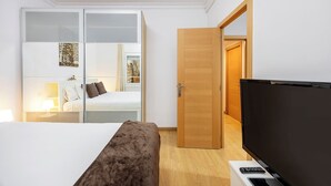 Hotellihuone, jossa on sänky, televisio, työpöytä kannettavalla tietokoneella, vaatekaappi ja ovi, joka johtaa toiseen huoneeseen.
