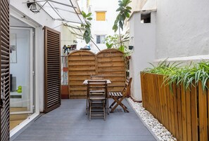 Eine schmale Außenveranda mit Holztisch und -stühlen, einem Holzzaun und Kübelpflanzen.