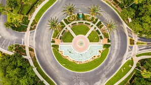 A circular intersection with a central fountain, surrounded by palm trees and greenery.