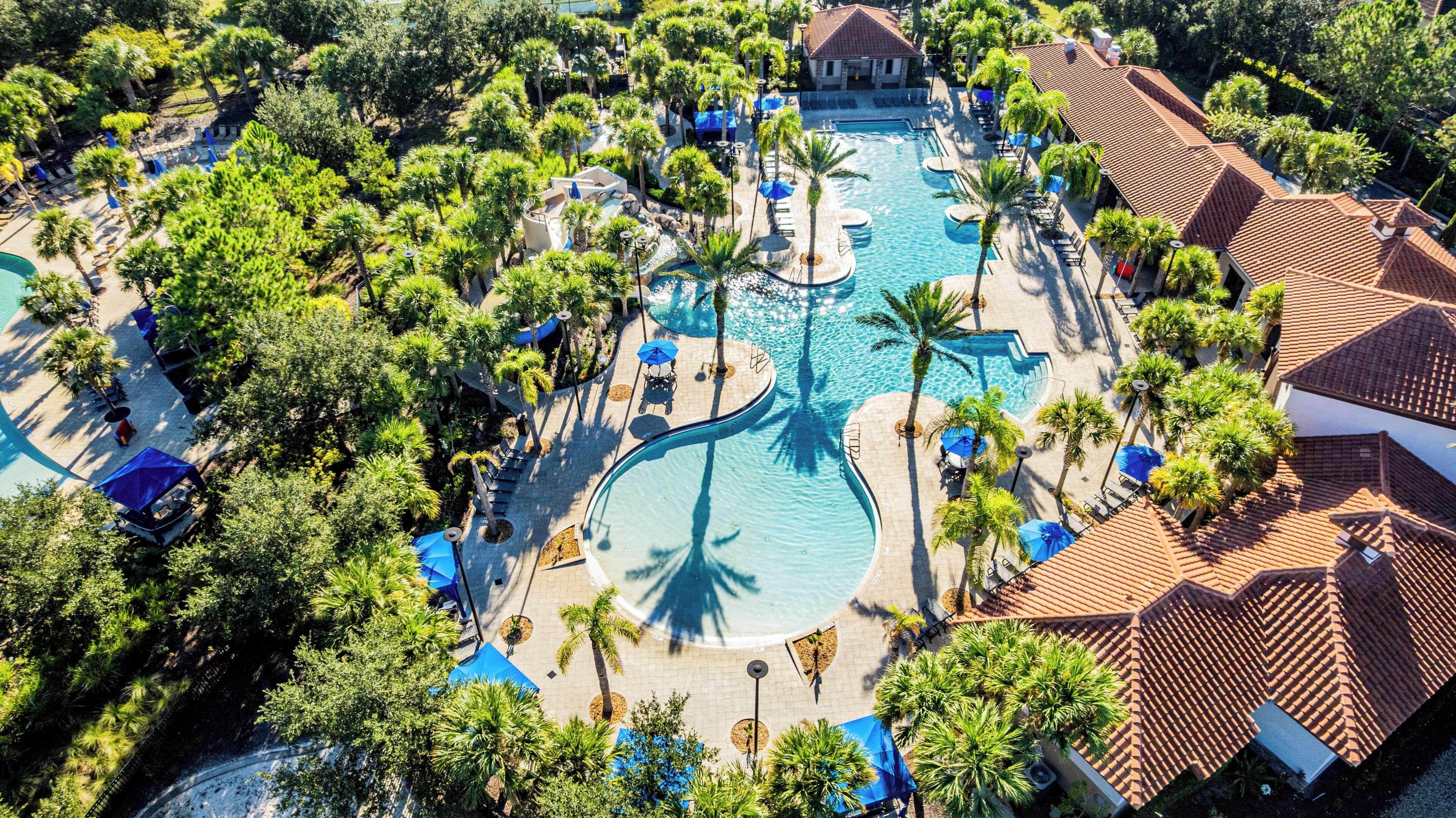 An aerial view of a resort with multiple swimming pools, palm trees, and lounge areas.